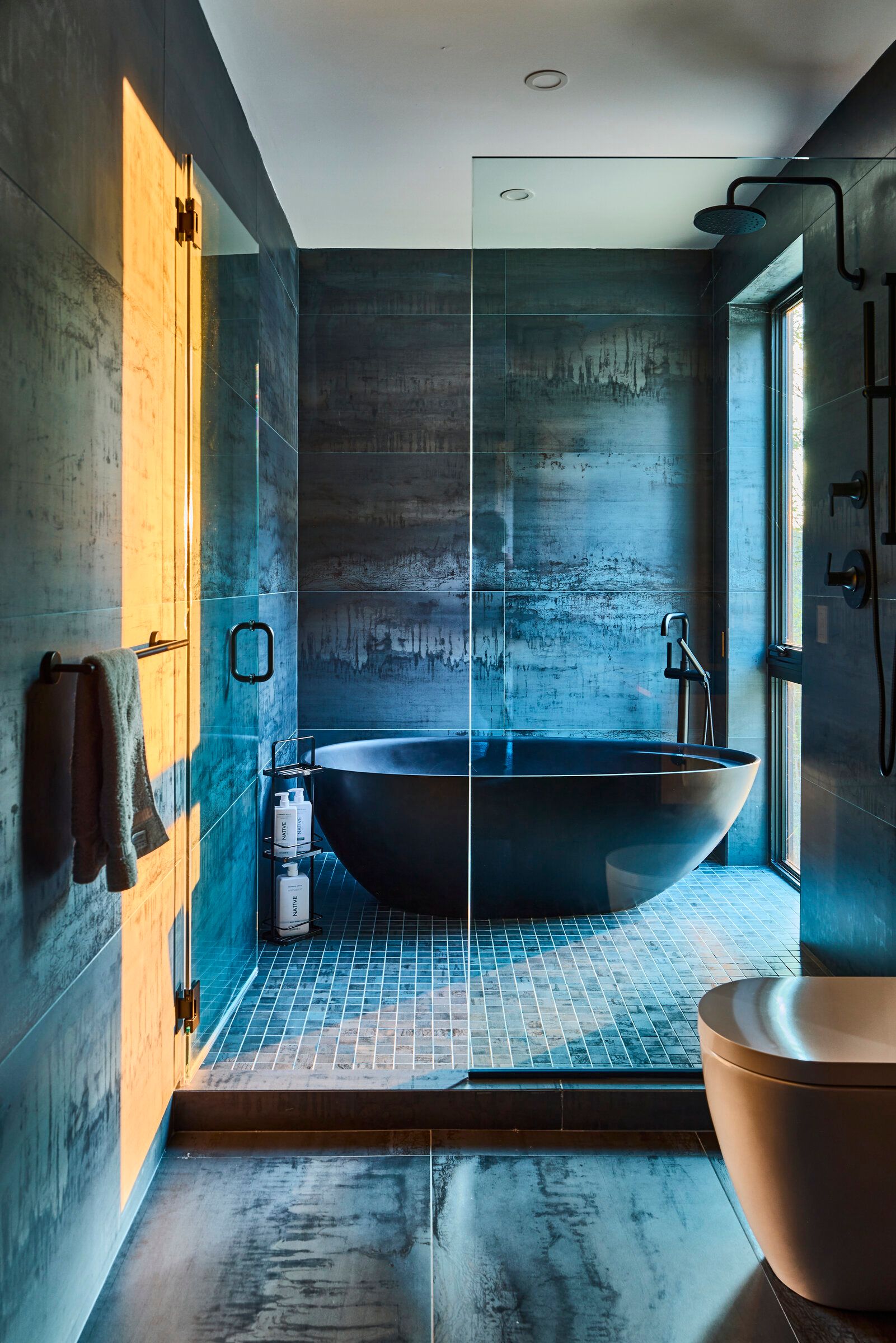 Verdant Sound primary bathroom — black soaking tub, raw concrete tile, glass shower