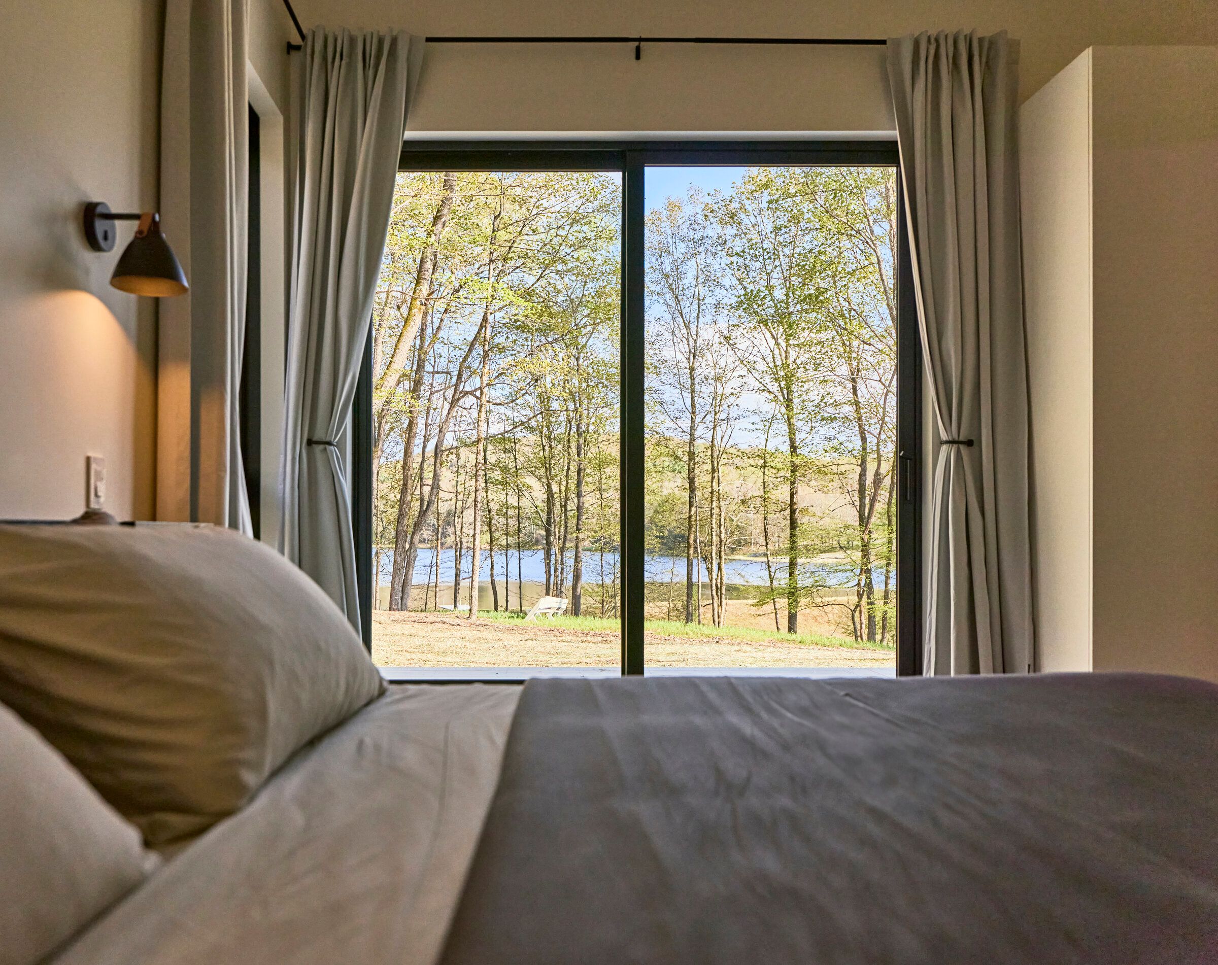 Bedroom at Verdant Sound — linen bed with a floor-to-ceiling window framing the private lake