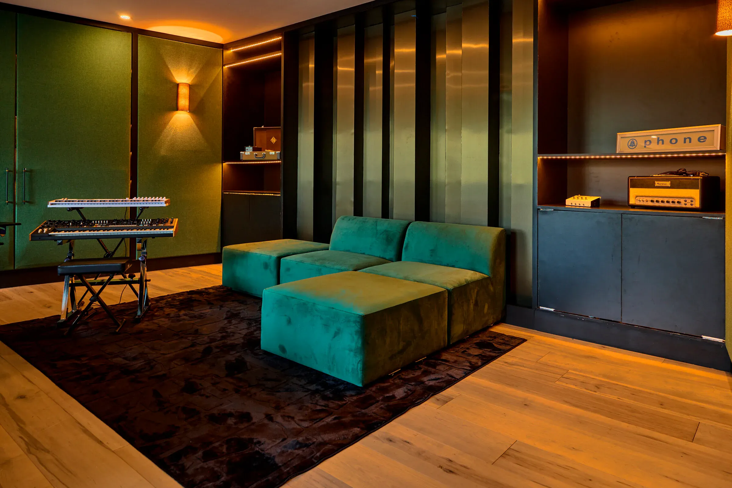 Verdant Sound control room lounge — green velvet sectional, synth rack, warm cove lighting
