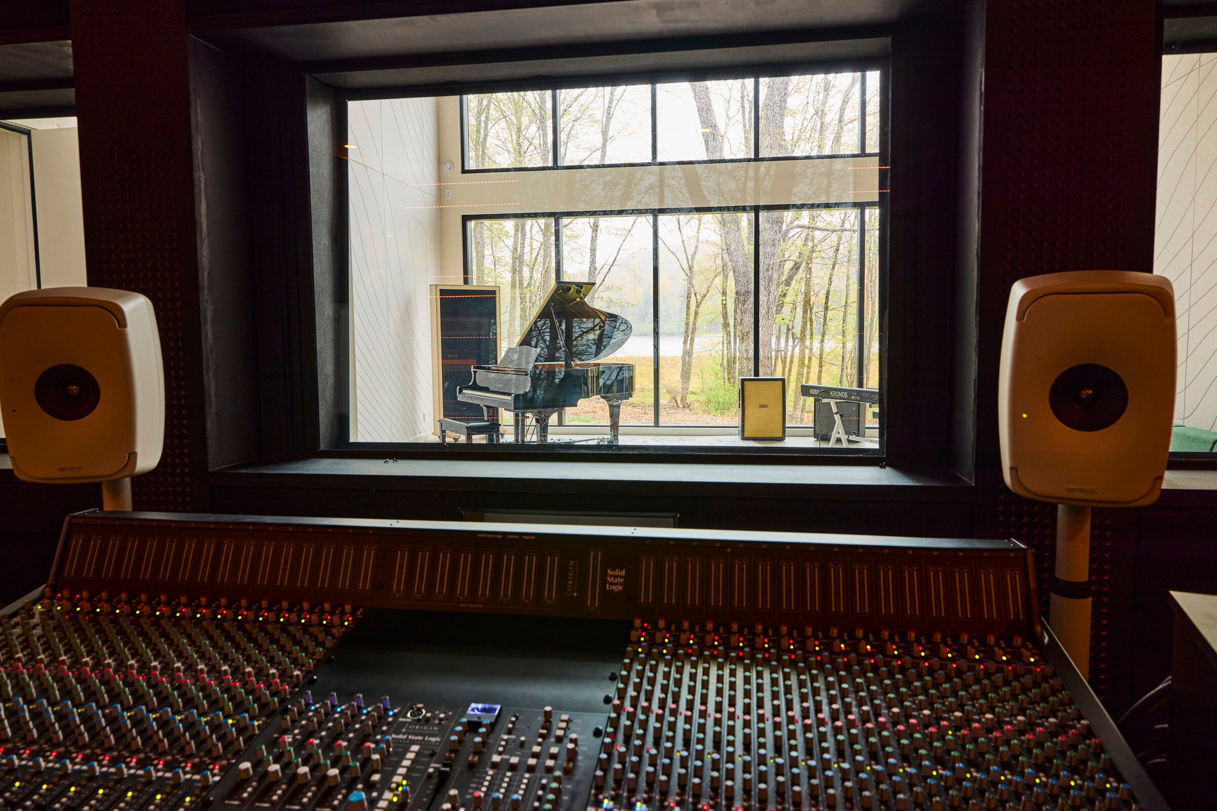 View from the Verdant Sound control room through the isolation glass into the live room — grand piano and lake