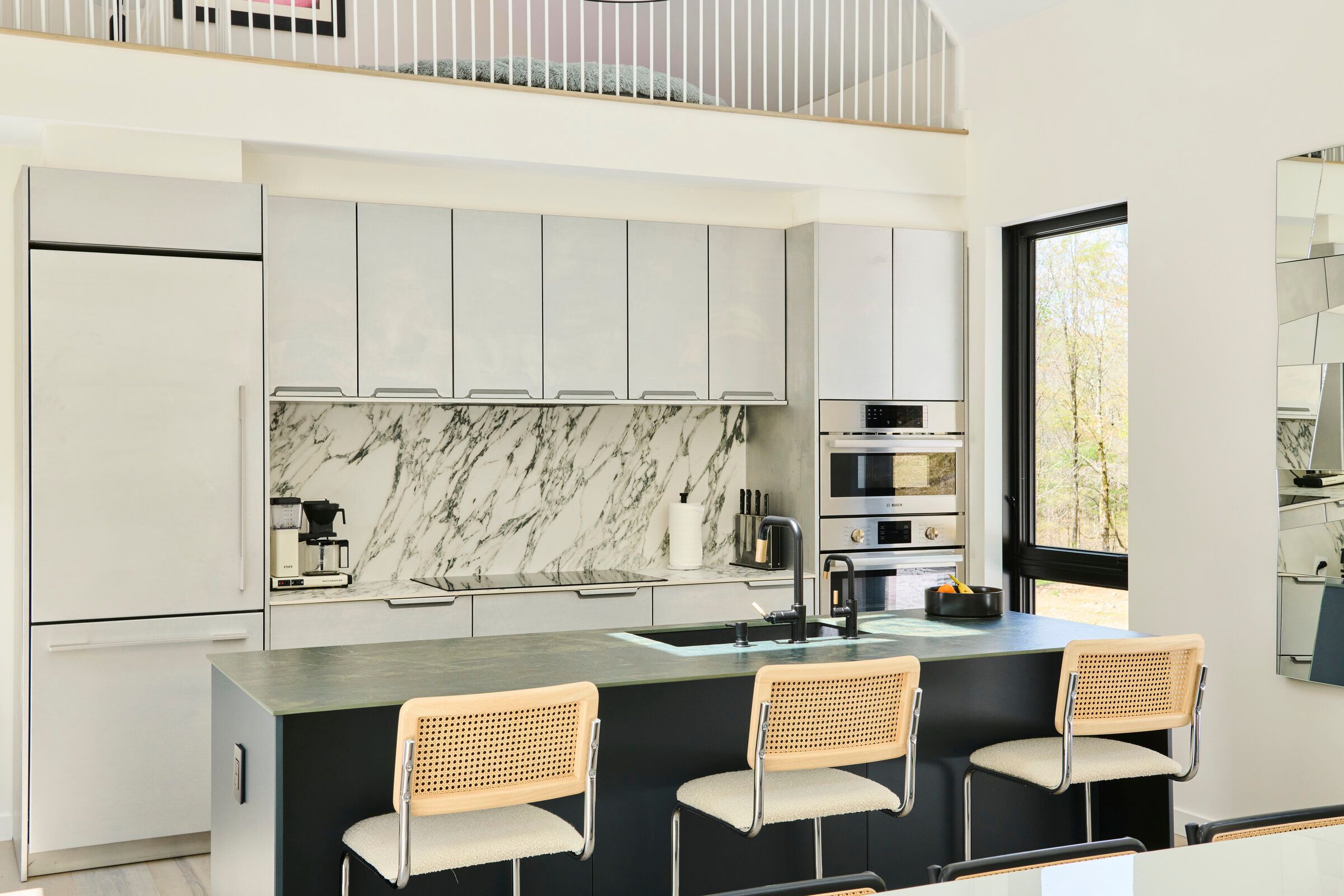 Verdant Sound kitchen — marble backsplash, grey cabinetry, and cane bar stools at the island