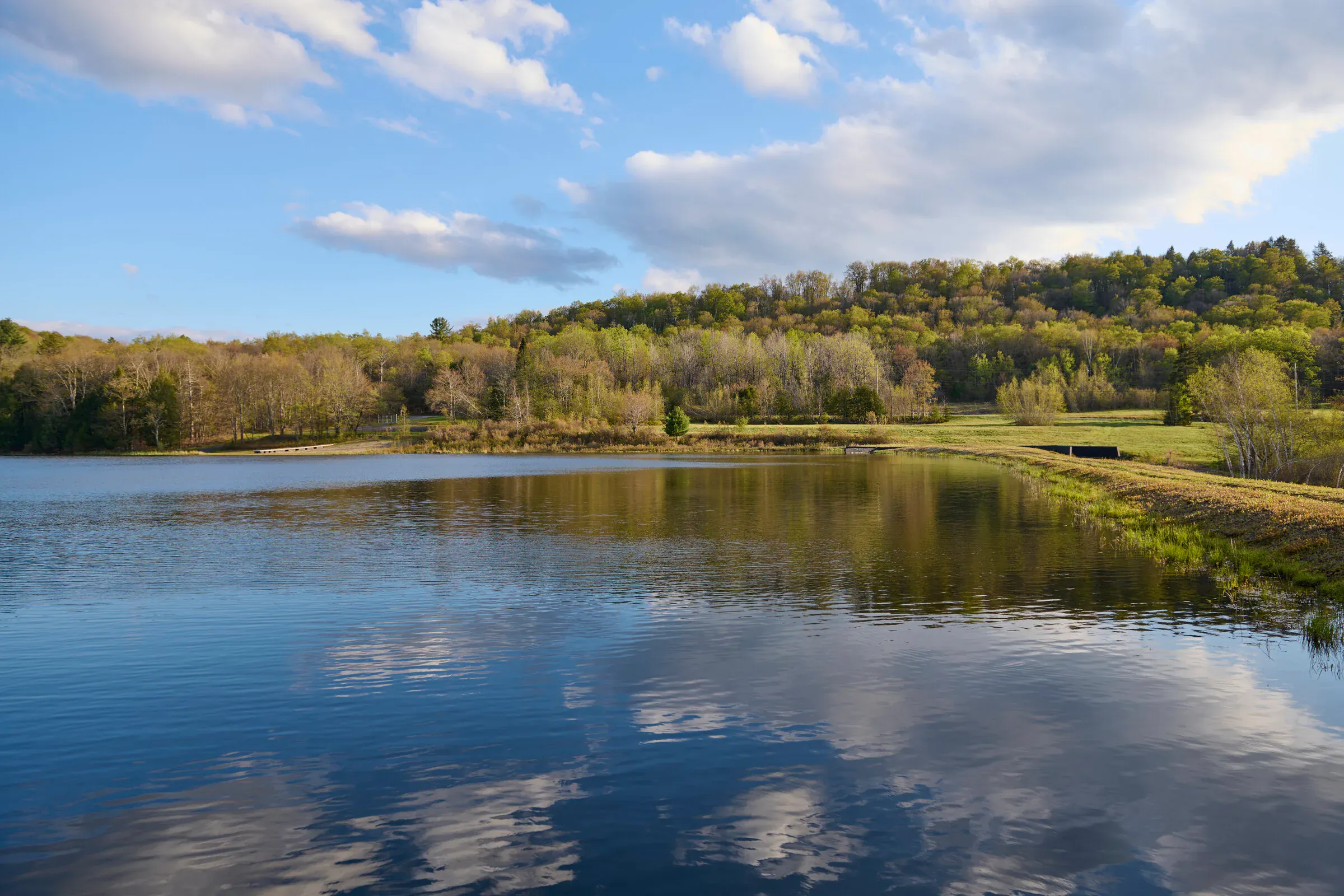 Private lake at Verdant Sound — wide view with clouds reflected on the water and rolling Catskills hills